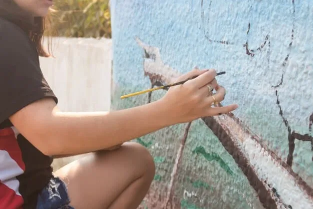 A close-up of a student carefully applying paint with a stencil on a school wall, demonstrating precision and focus in a graffiti art project.