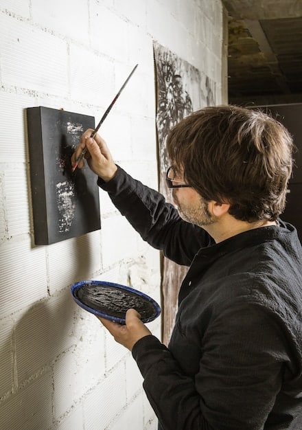 A collector examining an framed canvas graffiti piece in a minimalist gallery setting, highlighting the transition from street to curated spaces, focusing on the quality and framing of the artwork.