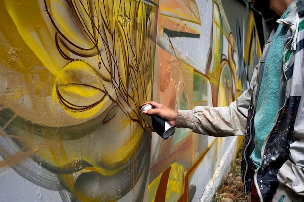 A detailed shot of an artist's hands working on a vibrant graffiti mural, holding a spray can with precision. The background shows blurred elements of the developing artwork and an urban street.