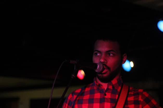 A close-up shot of a young US rapper adjusting the microphone on stage, looking intensely focused and ready to perform. The background is slightly blurred, highlighting the artist's anticipation.