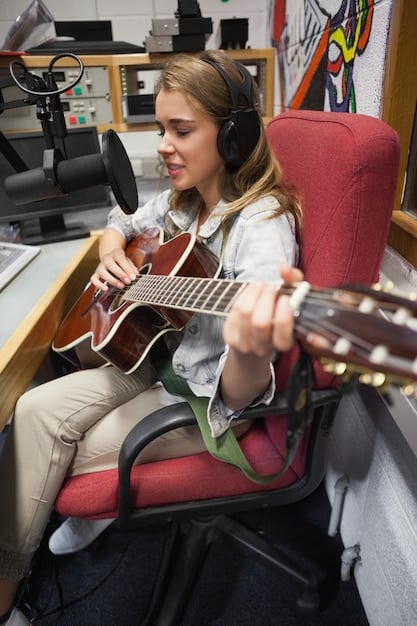 A music teacher in a classroom, showing a student how to use a sampler with a rap track in the background. The setting is a modern music lab with digital instruments and recording equipment.