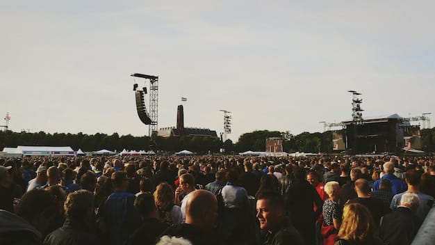A photograph of a large crowd gathered at an outdoor rap concert, with many people holding signs and banners protesting social injustice. The stage is visible in the background, with a rapper performing passionately. The overall atmosphere is energetic and charged with a sense of purpose.