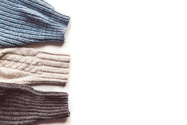 A detailed flat lay of various streetwear garments for layering, demonstrating different textures and lengths, including a graphic tee, an open plaid flannel, a denim jacket, and a beanie, all in complementary muted tones, arranged neatly.