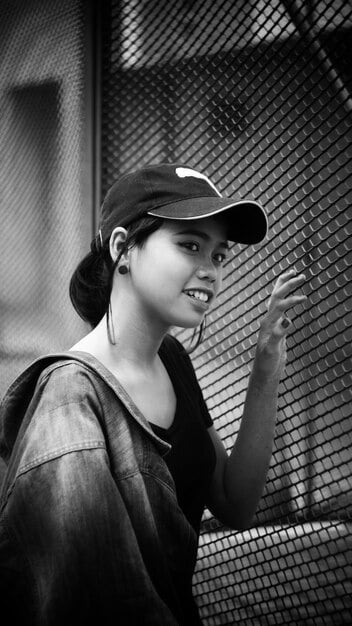A close-up of a stylish individual wearing a black baseball cap with intricate white embroidery, tilted slightly, complementing a monochrome streetwear outfit in an urban alleyway.