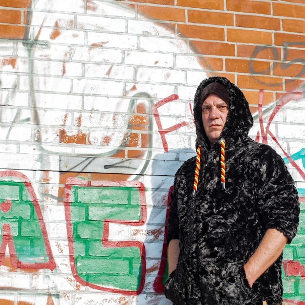A close-up shot of a streetwear hoodie featuring intricate embroidery and vibrant graffiti-style artwork, with a blurred urban backdrop of brick walls and faint tagging.