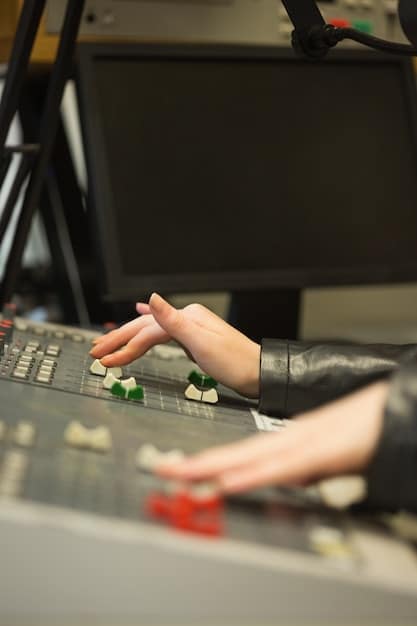 A close-up side view of a musician's hand adjusting knobs on a multi-track loop station, surrounded by other music equipment, in a home studio environment.