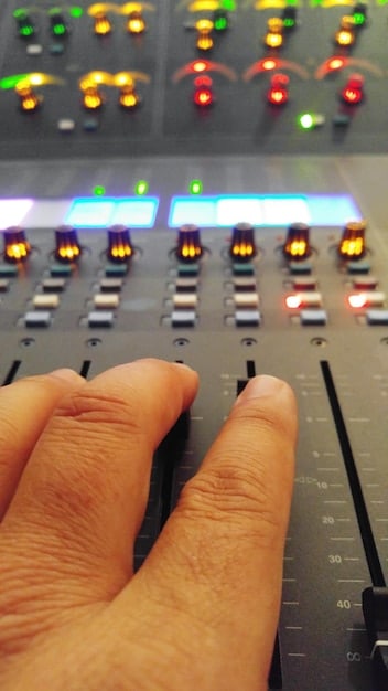 A detailed close-up of a producer's hand on a mixing board, with illuminated knobs and faders, surrounded by synthesizers and studio monitors, illustrating the hands-on process of sound design and music production.