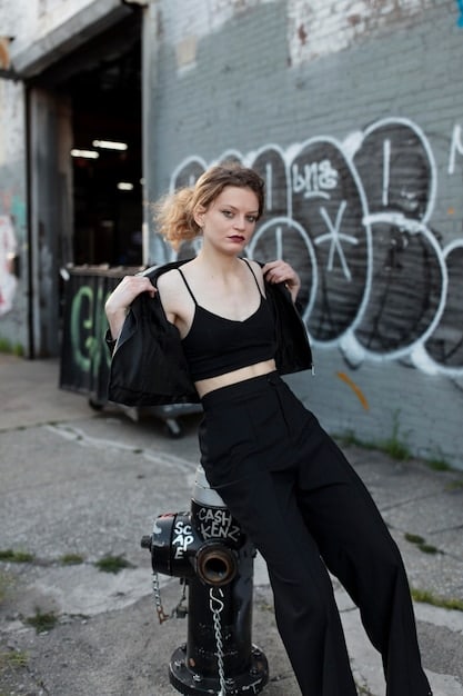 A stylish model effortlessly pulling off a cropped streetwear look. They are wearing a black cropped hoodie with exaggerated dropped shoulders, paired with high-waisted, wide-leg beige cargo pants. The composition highlights the silhouette, showing how the cropped top accentuates the long lines of the pants. The background is minimalist and industrial.